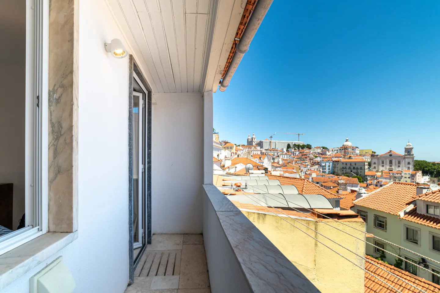 Balcony view of Lisbon, Portugal. White walls, marble trim, and red tile roofs under a clear blue sky.
