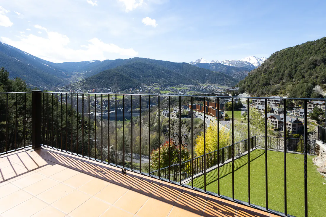 Balcony view with black iron railing, tan tile, and green turf. Mountains, trees, and buildings are in the background.