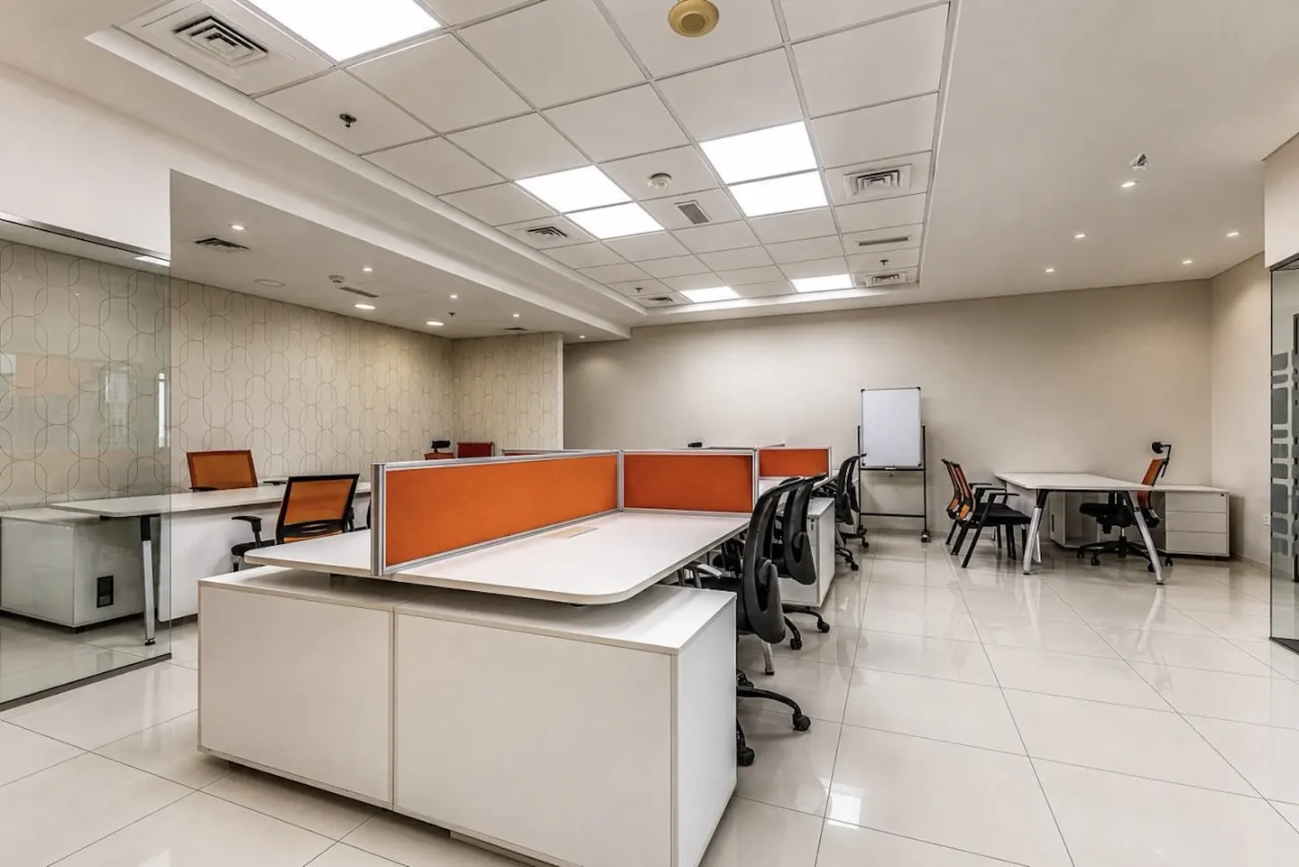 Bright office space with white desks, orange dividers, and black chairs on a tiled floor. A whiteboard stands in the background.