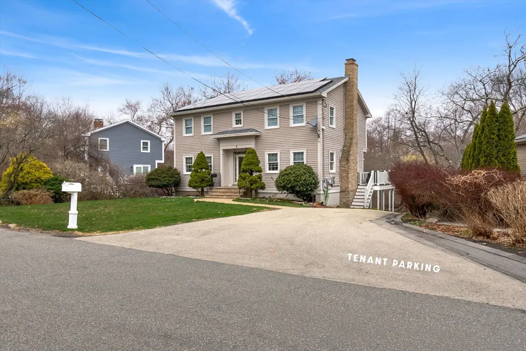 Two-story beige house with solar panels and a brick chimney, viewed from the street. "Tenant Parking" is painted on the driveway.