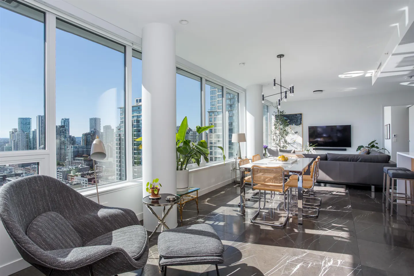 Bright, modern condo interior with a gray chair, dining table, and city view through large windows.