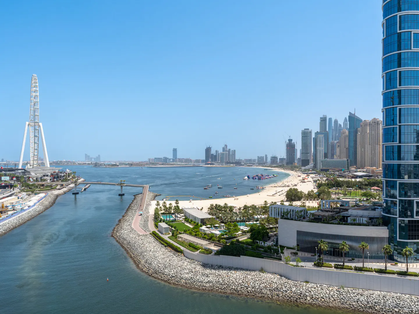 Dubai skyline view with Ain Dubai Ferris wheel, beach, and skyscrapers under a clear blue sky.