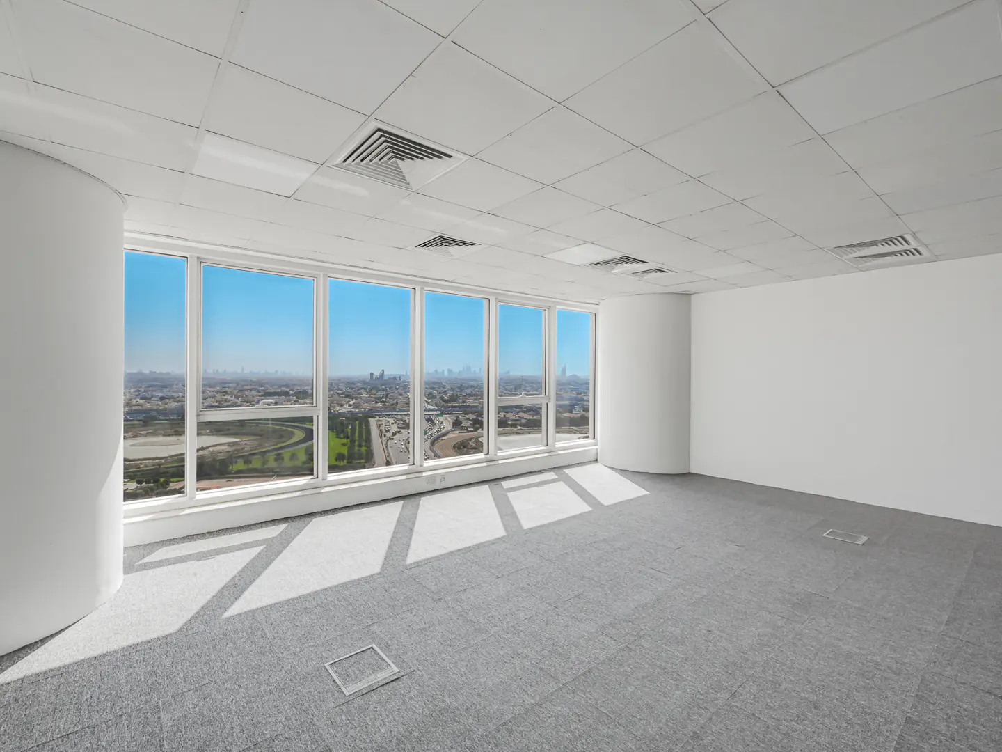 Bright, empty office space with gray carpet, white walls, and large windows overlooking a city skyline.
