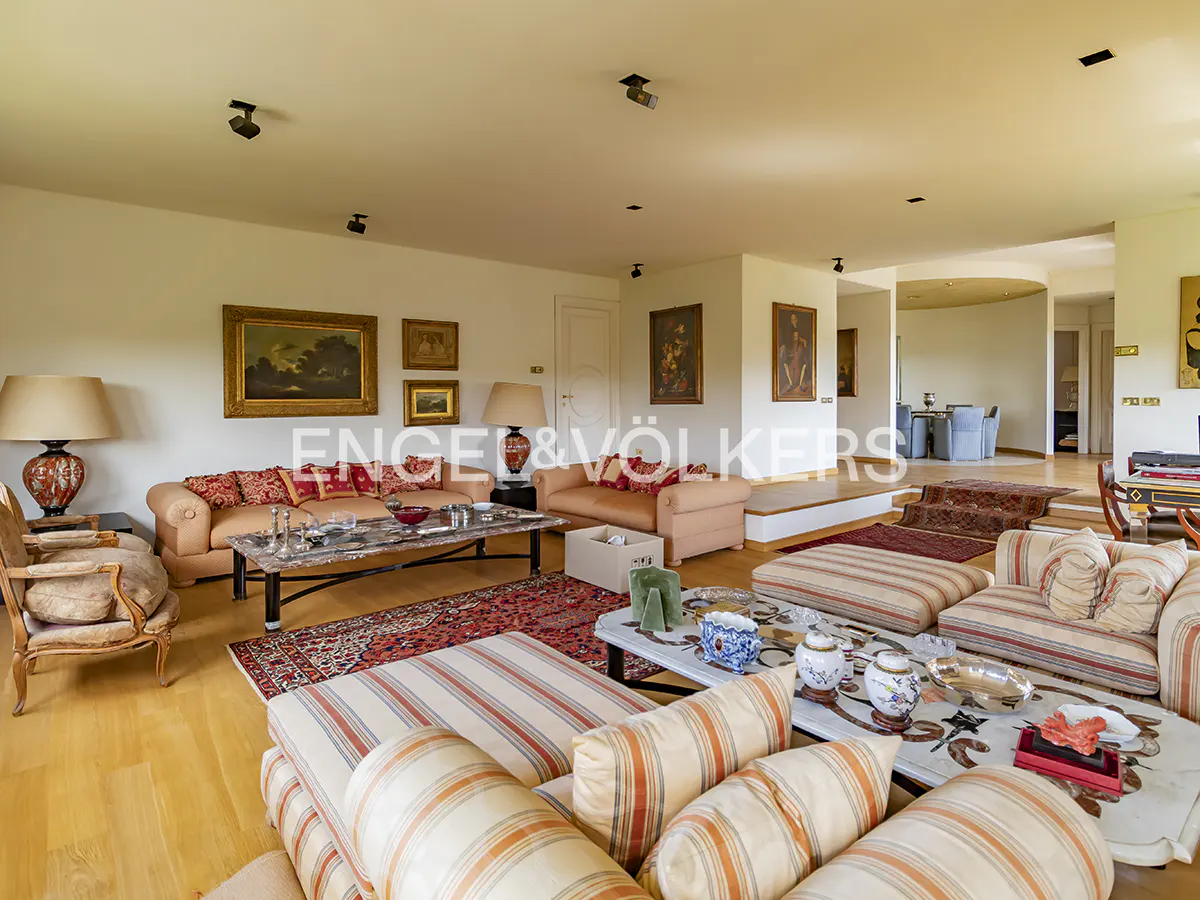 A spacious living room with sofas, art, and wooden floors. The room is well-lit with natural light.