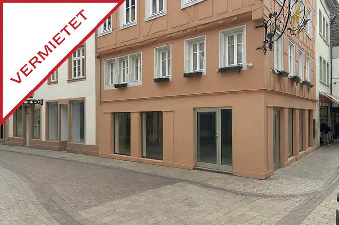 Exterior of a peach-colored, multi-story building with white-framed windows and a red "VERMIETET" sign.