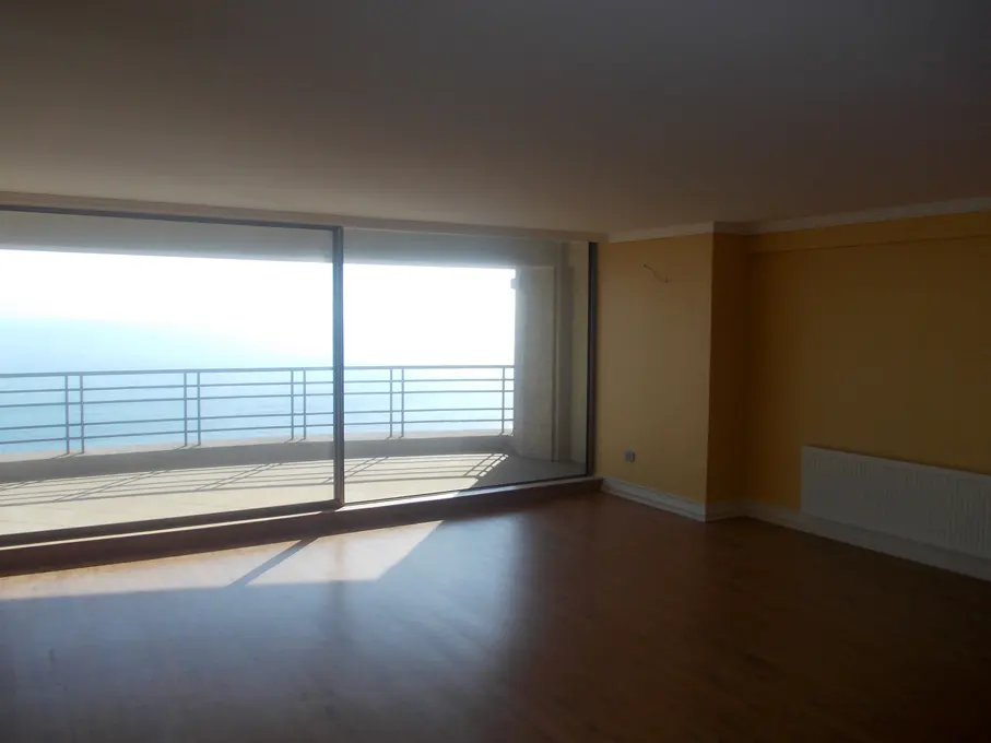 Empty room with wood floors, yellow walls, and a sliding glass door to a balcony overlooking the ocean.