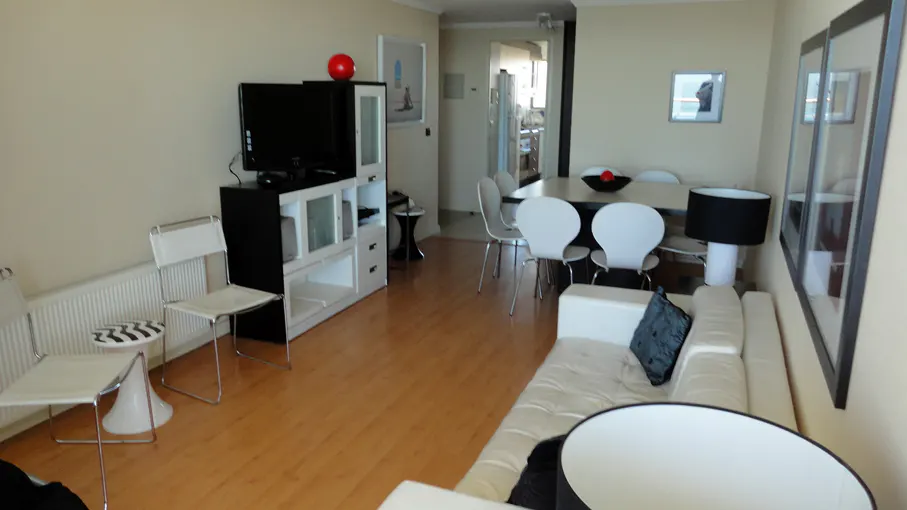 Living room with wood floors, white sofa, dining table with white chairs, and a black TV stand with a red ball on top.