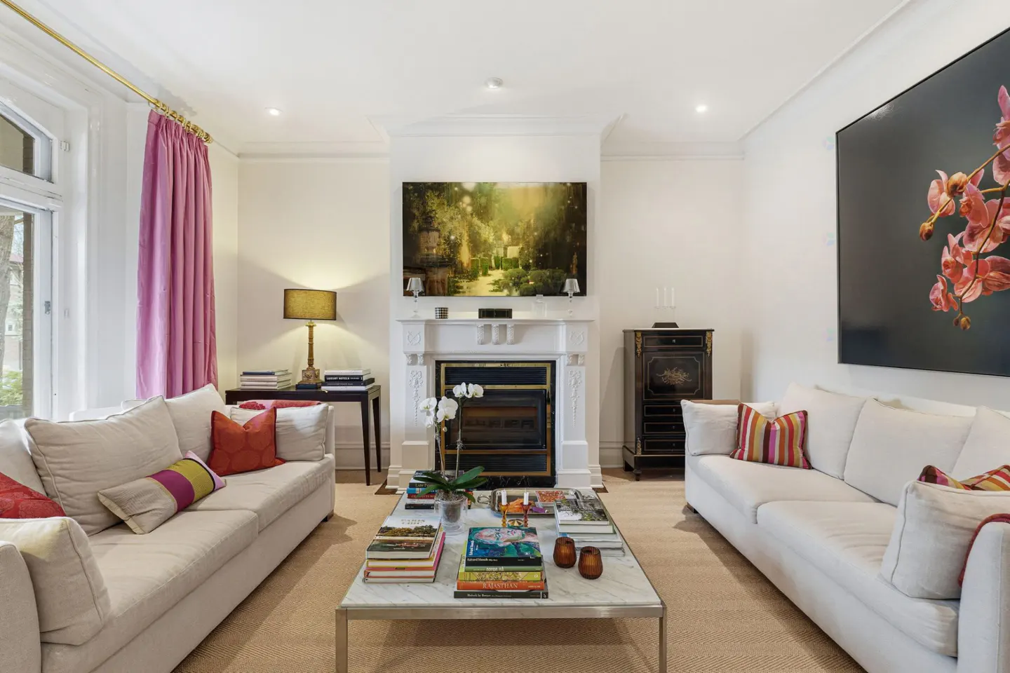 Bright living room with two white sofas facing each other, a marble coffee table, and a fireplace with a painting above it.