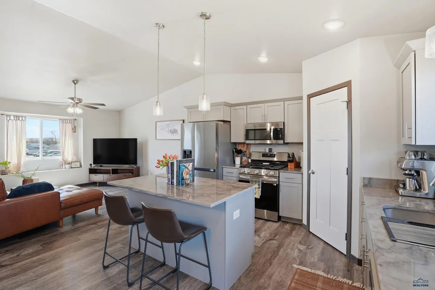 Open-concept living space with gray cabinets, stainless steel appliances, and a brown leather couch.