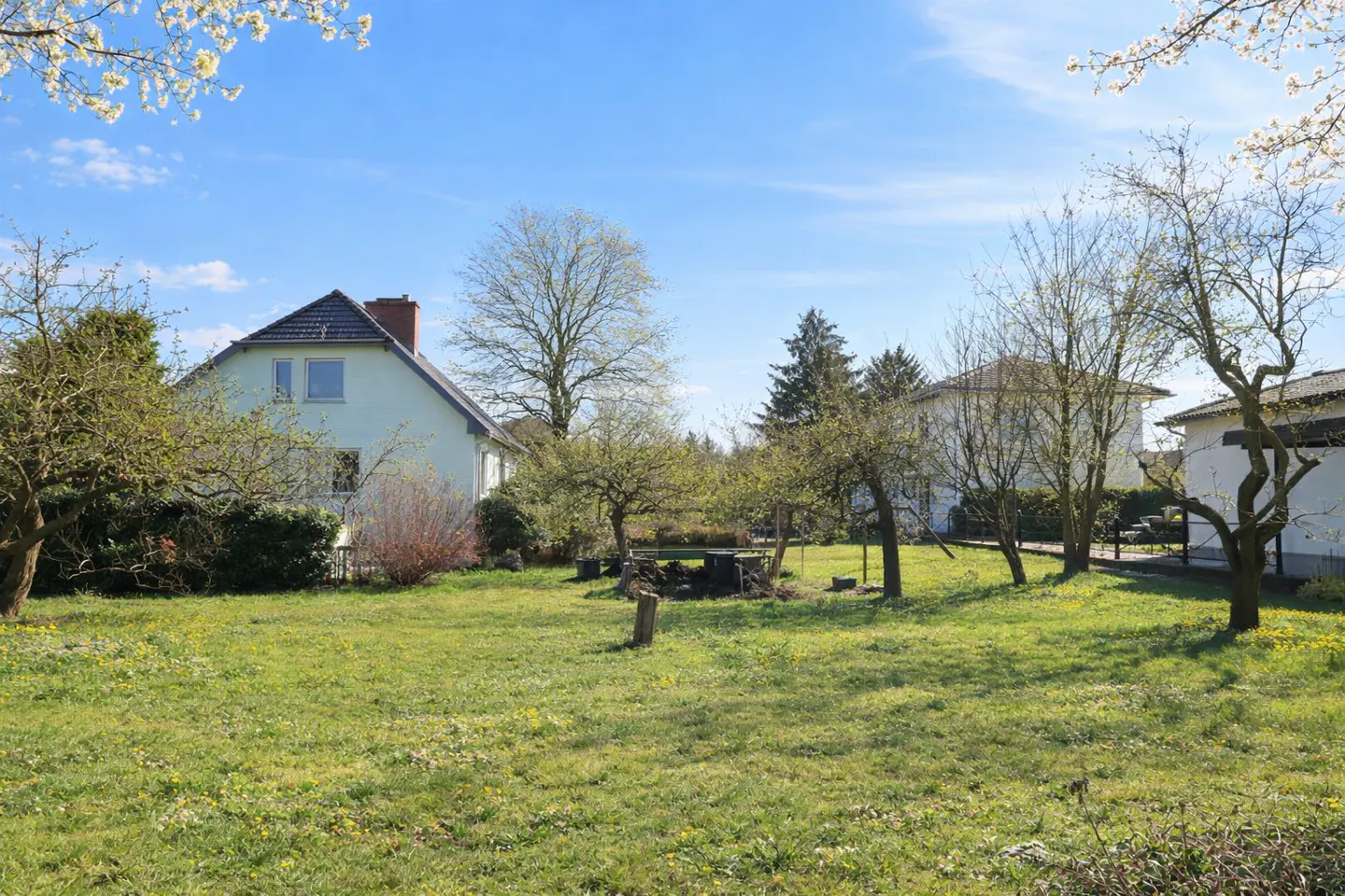 A house with a large green lawn and trees under a blue sky.