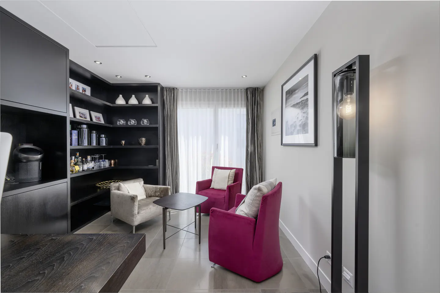 Living room with dark wood shelves, red armchairs, and a floor lamp. A framed picture hangs on the wall.