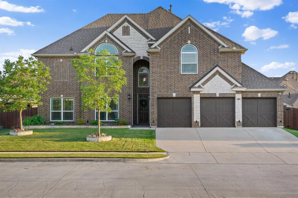 Two-story brick house with a three-car garage, arched windows, and a well-manicured lawn on a sunny day.