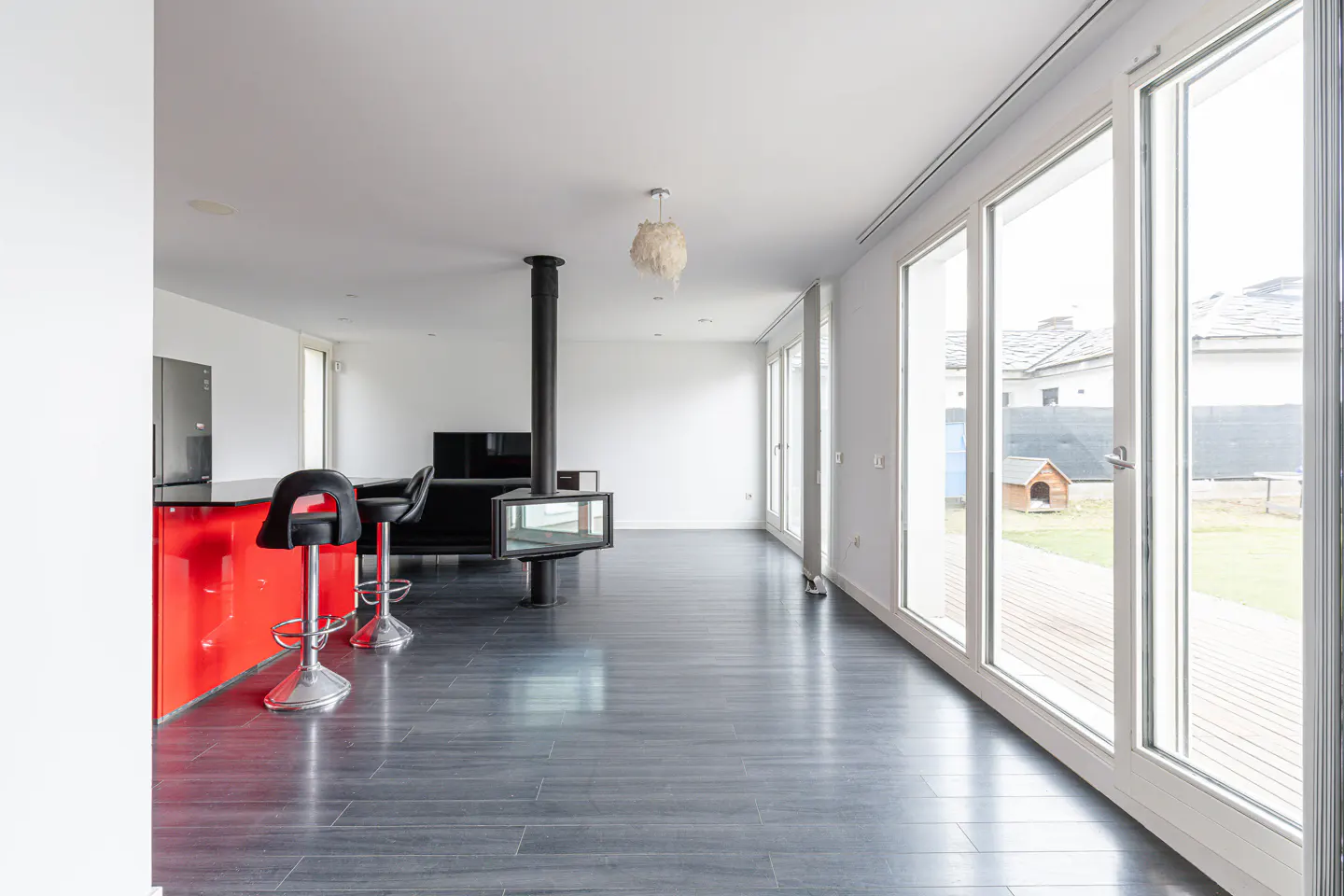 Bright, modern living room with a red bar, black stools, and a suspended fireplace. Large windows offer a view of the yard.