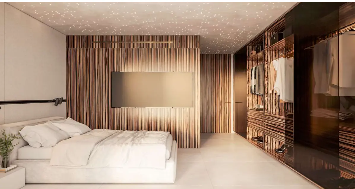Bedroom with white bed, wood-paneled wall with TV, and closet. Ceiling has star-like lights.