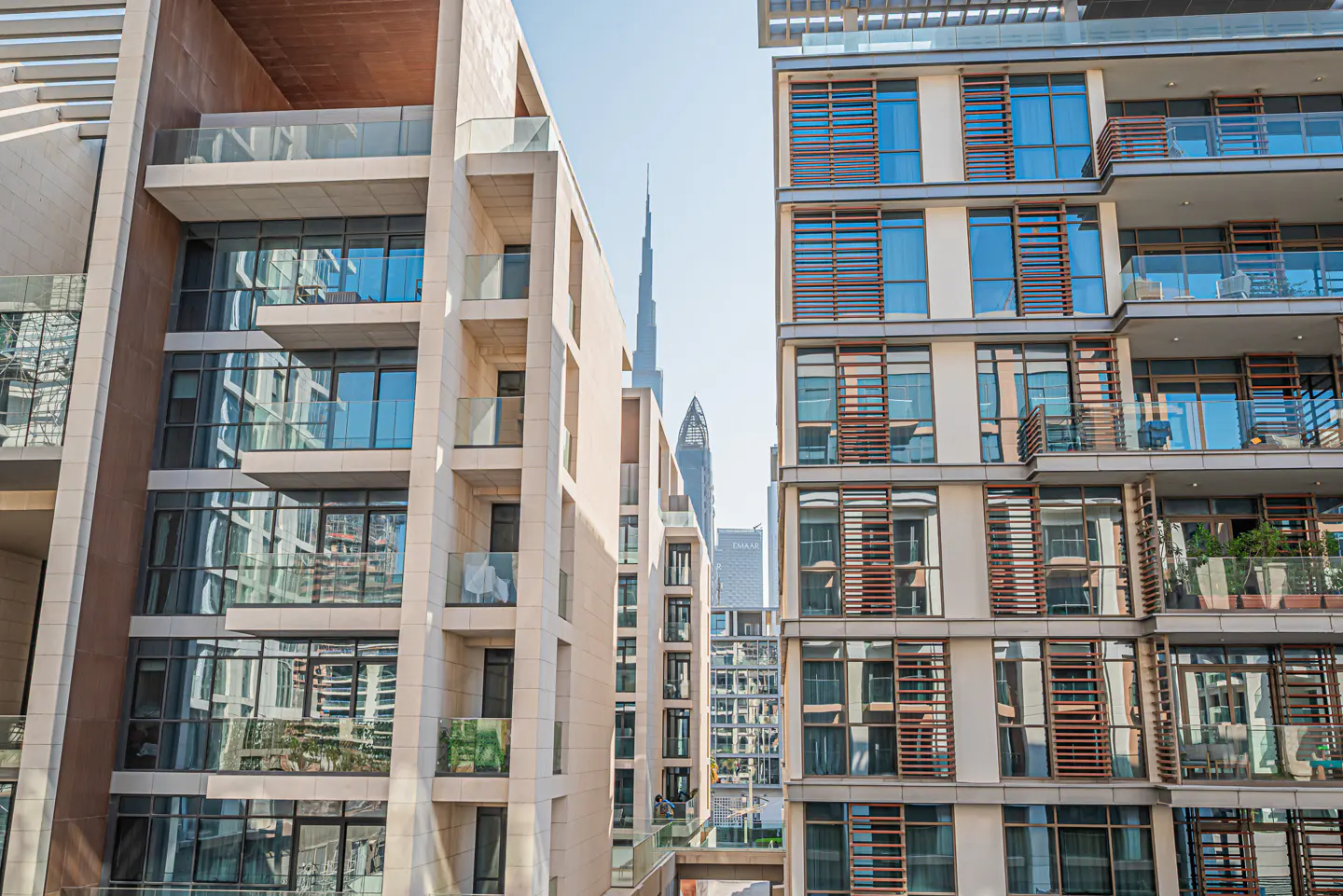 Exterior view of modern beige apartment buildings with balconies and large windows, with the Burj Khalifa in the background.