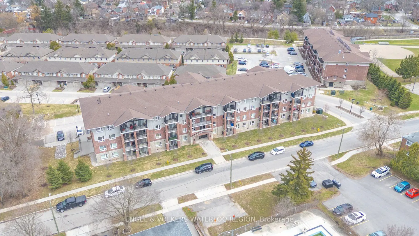 Aerial view of a brick and gray apartment building with balconies, surrounded by trees and parked cars.
