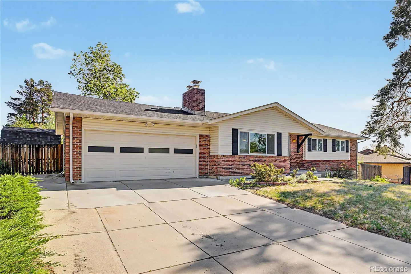A single-story brick house with a white garage door and a concrete driveway under a blue sky.