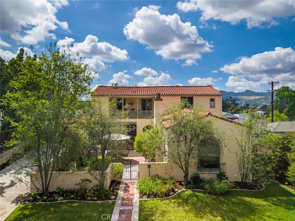 Two-story peach house with a red tile roof, green trees, and a blue sky with white clouds.