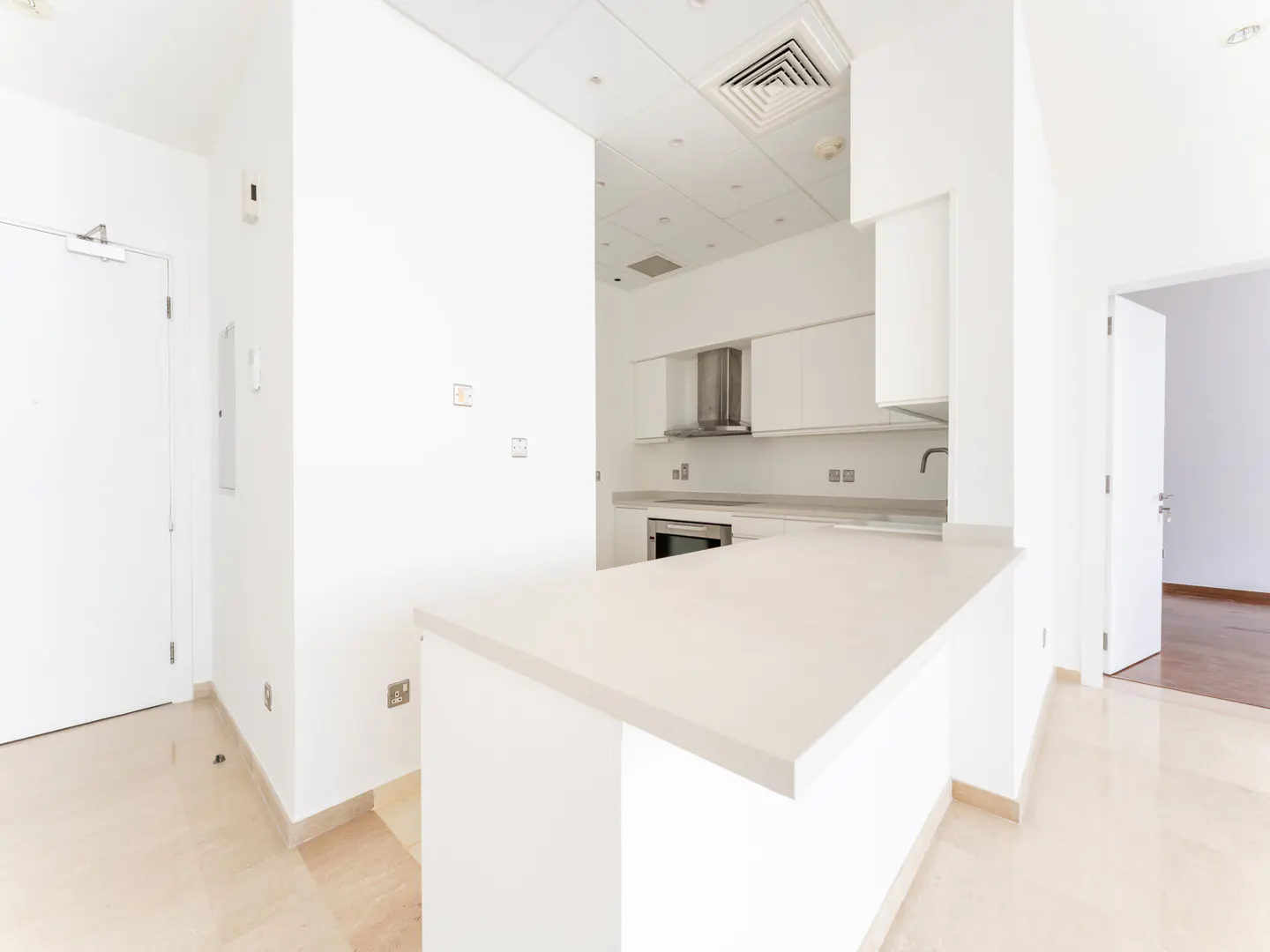 Bright, modern kitchen with white cabinets, countertops, and walls. A breakfast bar separates the kitchen from the living area. A doorway leads to another room.