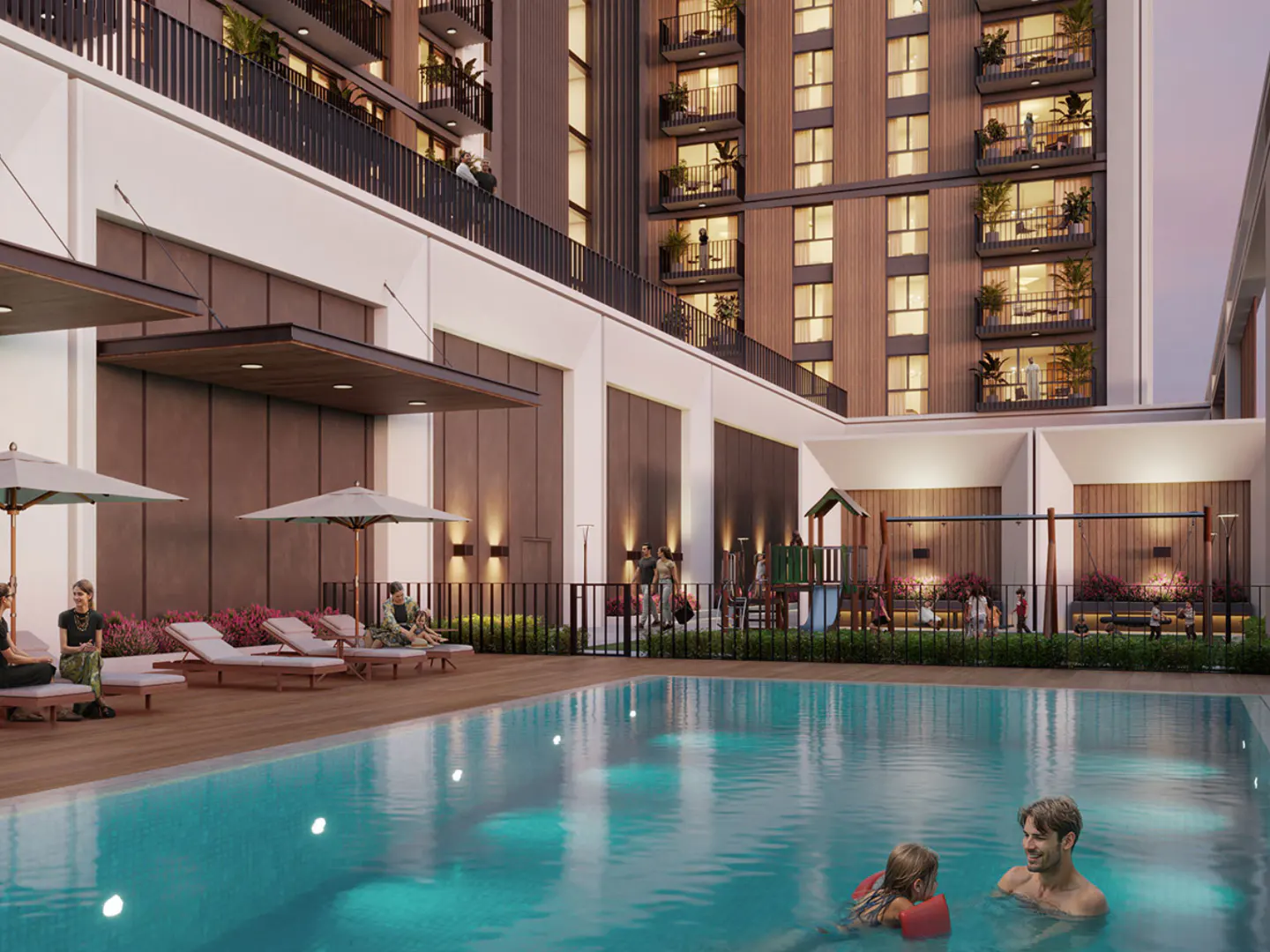 Outdoor pool area with a man and child swimming. Lounge chairs and umbrellas line the pool deck. A playground and apartment building are in the background.