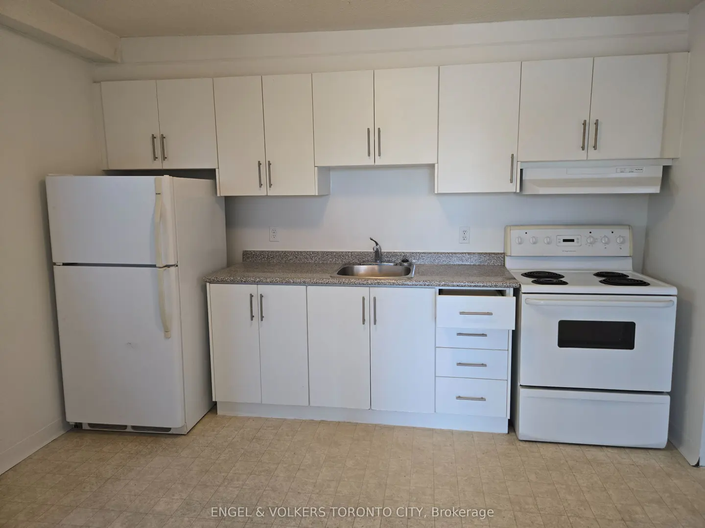 Kitchen with white cabinets, white appliances, a speckled grey countertop, and a light-colored tiled floor.