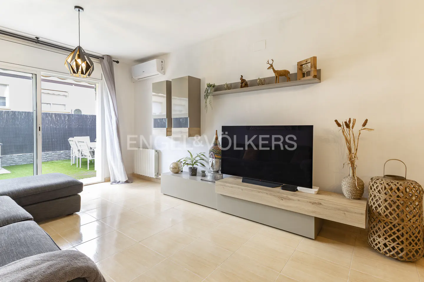 A bright living room with a gray sofa, TV, and sliding glass doors to a green lawn.