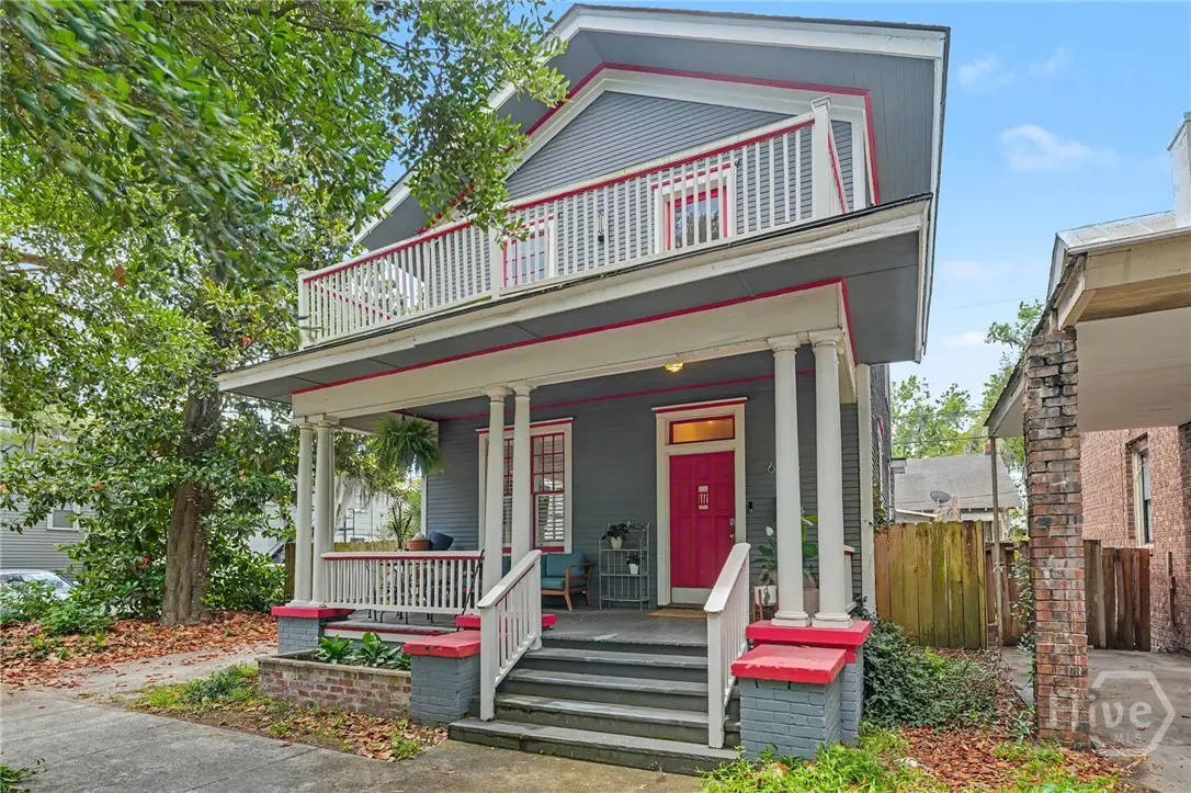 Two-story gray house with white trim and a red door. A porch and balcony are visible.