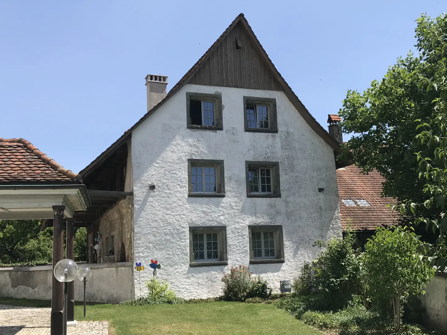 Exterior view of a white, two-story house with a brown roof and trim, surrounded by green grass and trees.