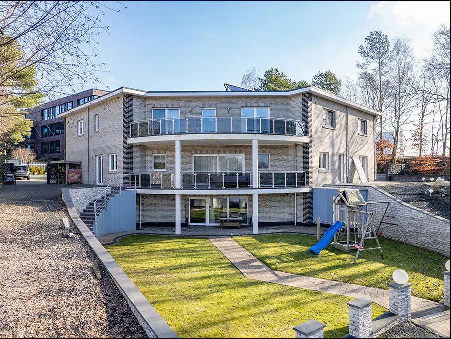 Three-story gray brick building with balconies overlooking a green lawn and a blue slide.