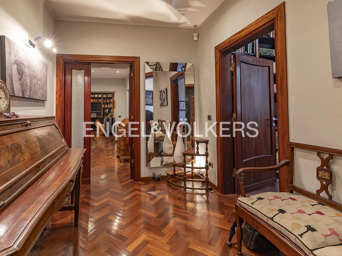 Hallway with herringbone wood floors, wood trim, and a vintage desk. A mirror reflects the hallway. A bench sits to the right.