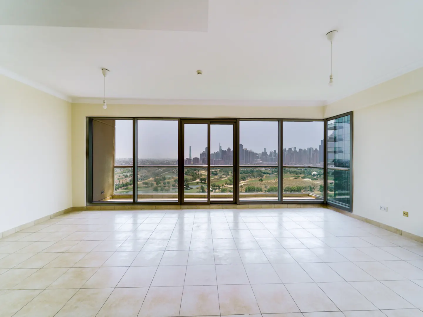 Empty room with tile floor and large windows showing a city skyline and green space.