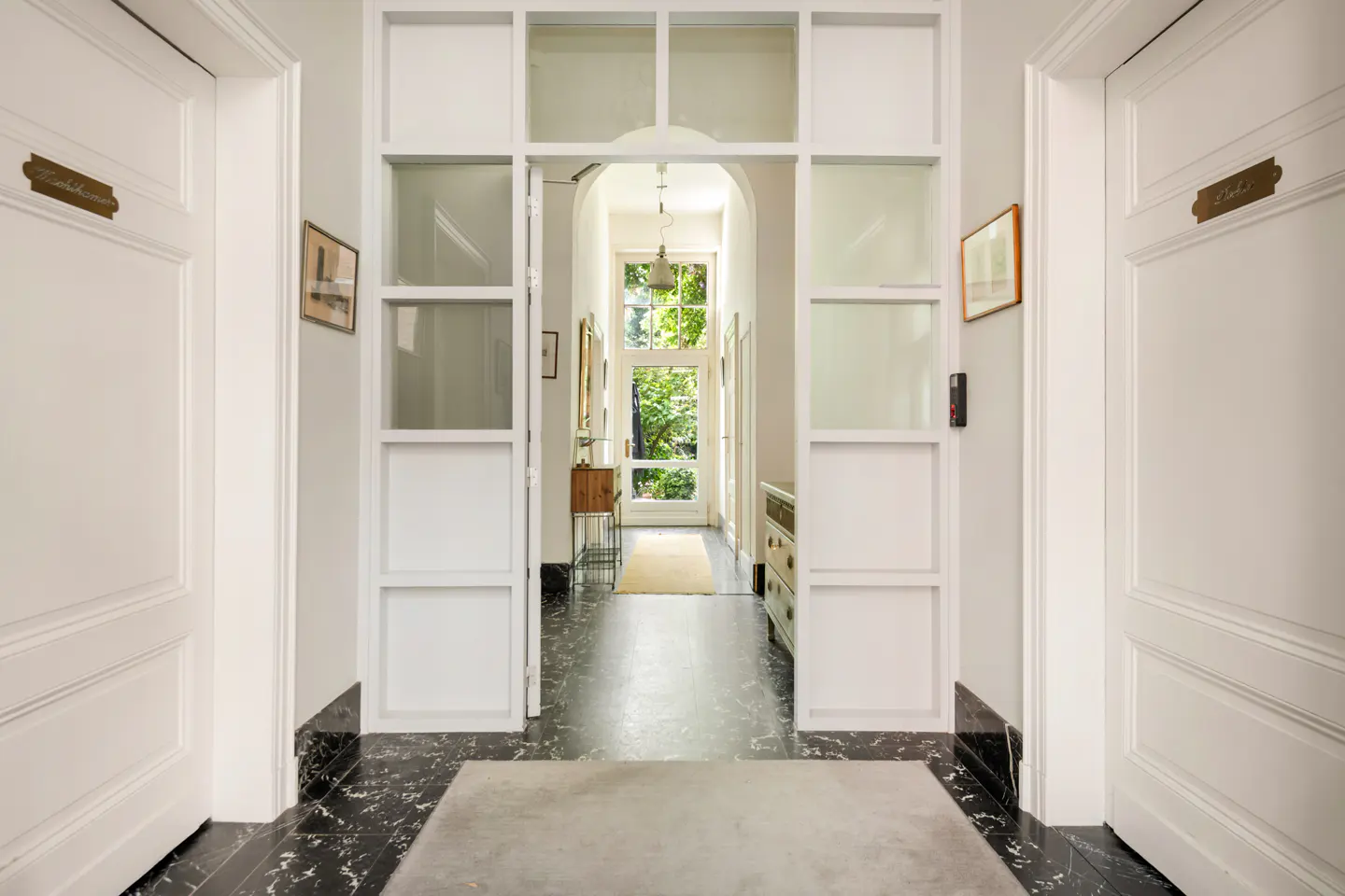 Hallway with black marble floors, white walls, and white doors. A glass door leads to a bright outdoor view.