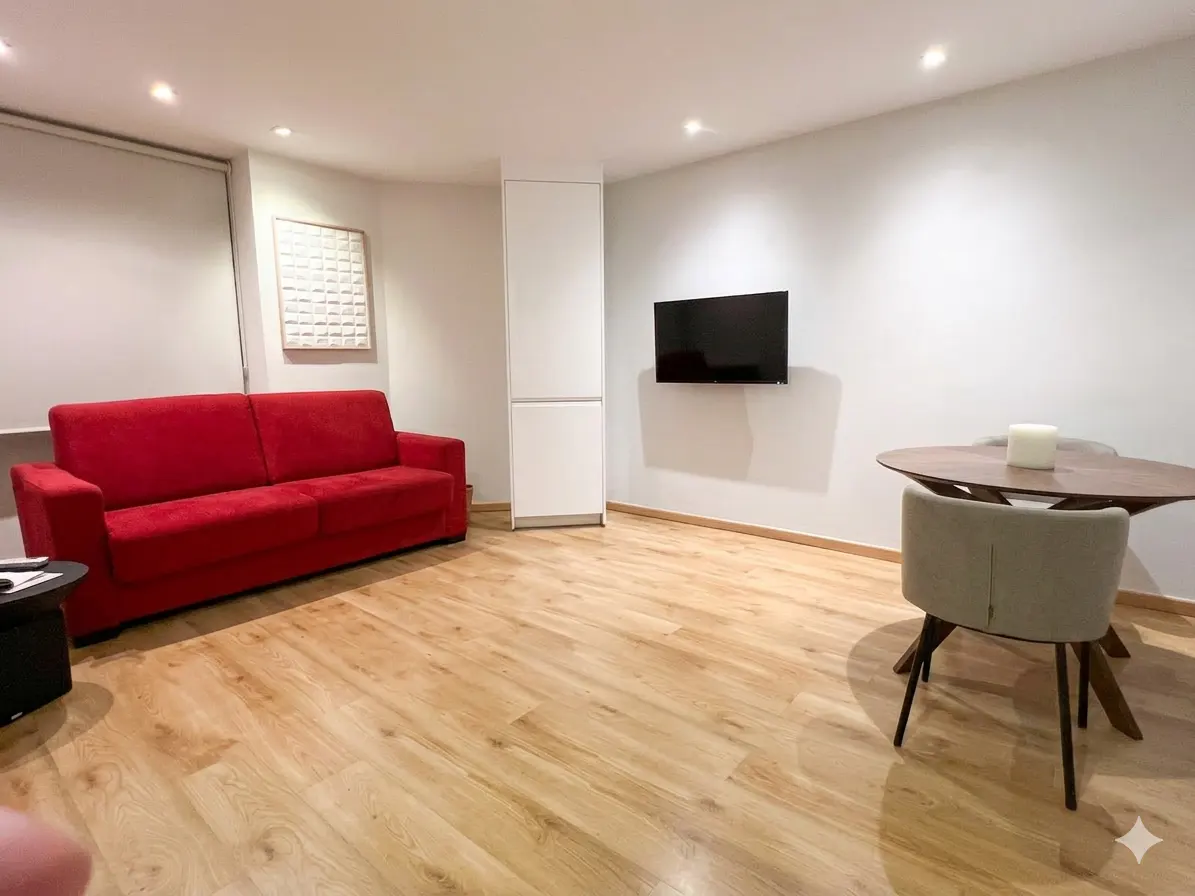 Living room with a red sofa, wood floors, a round table with chairs, and a wall-mounted TV.