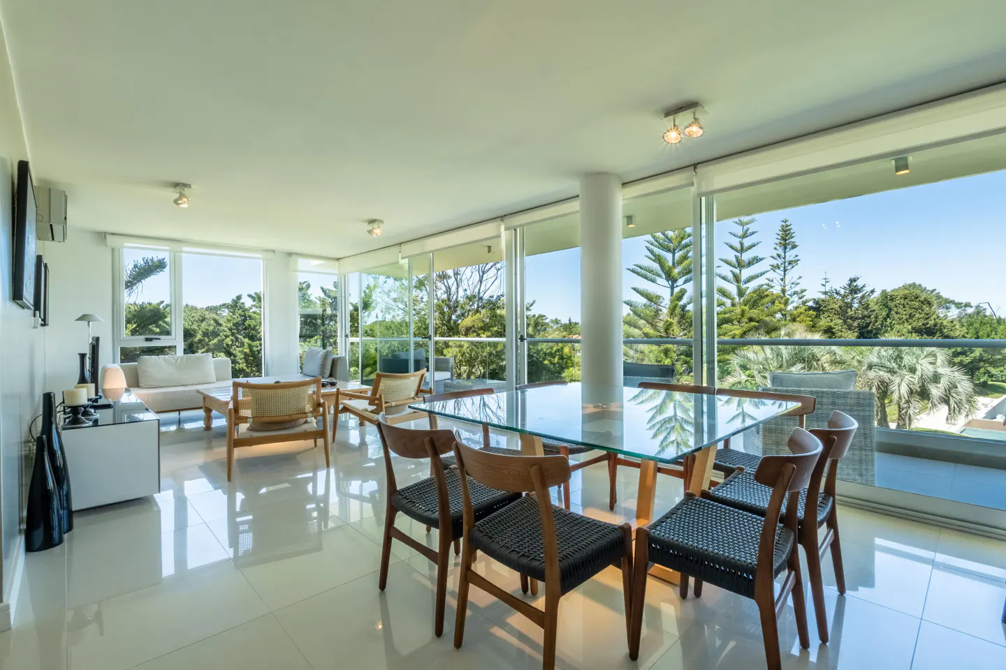 Modern dining area with a glass table, black chairs, and floor-to-ceiling windows overlooking a lush, sunny garden.