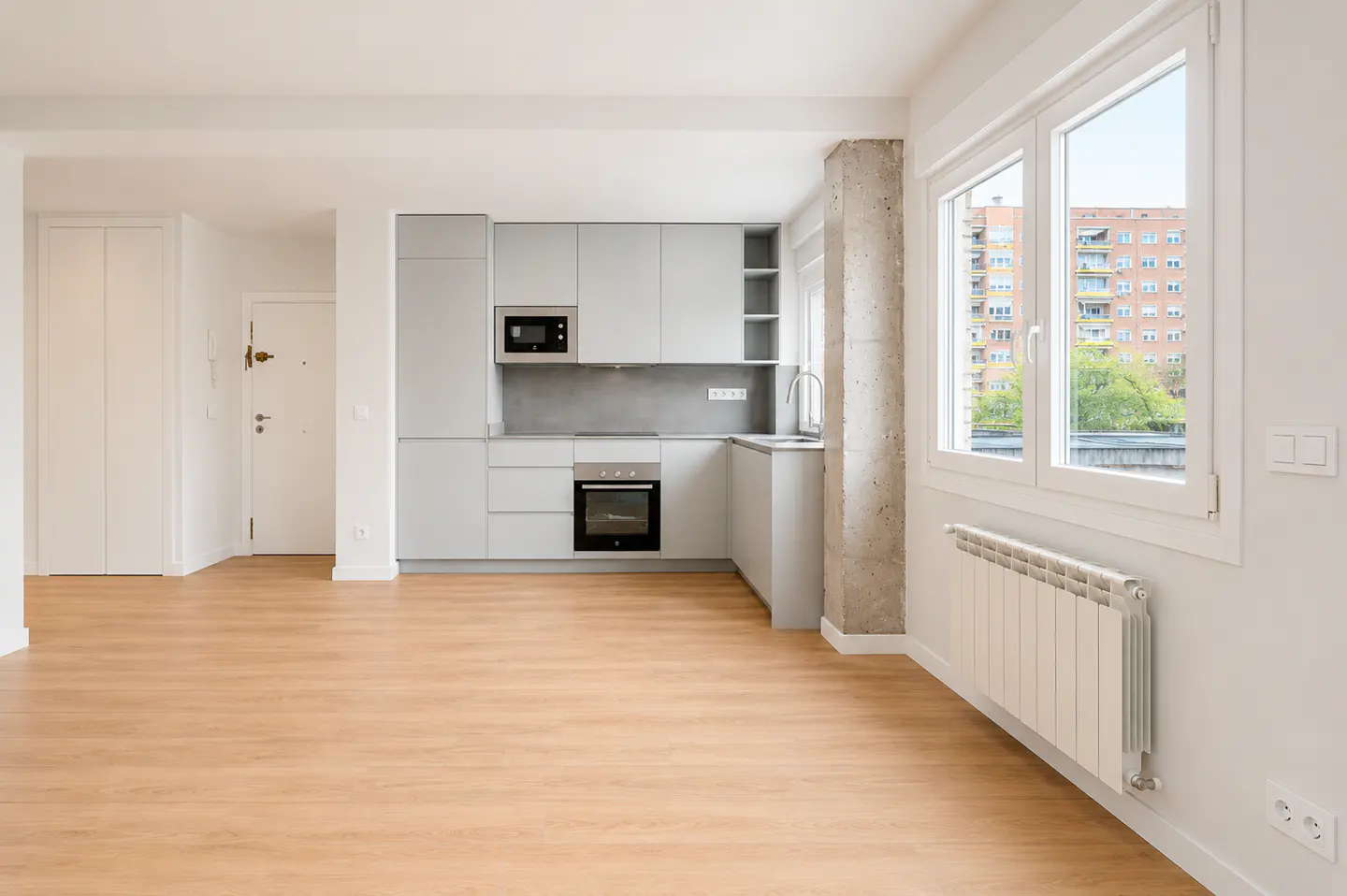 Modern kitchen with light grey cabinets, wood floors, and a window view of an apartment building.