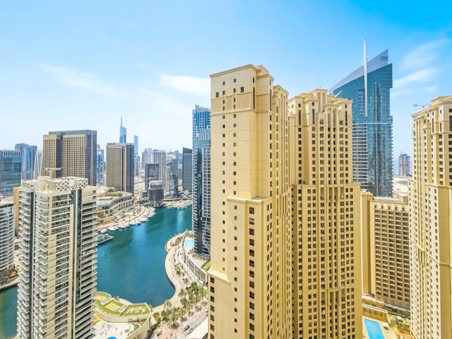 View of Dubai Marina with beige skyscrapers, a blue canal, and a clear blue sky.