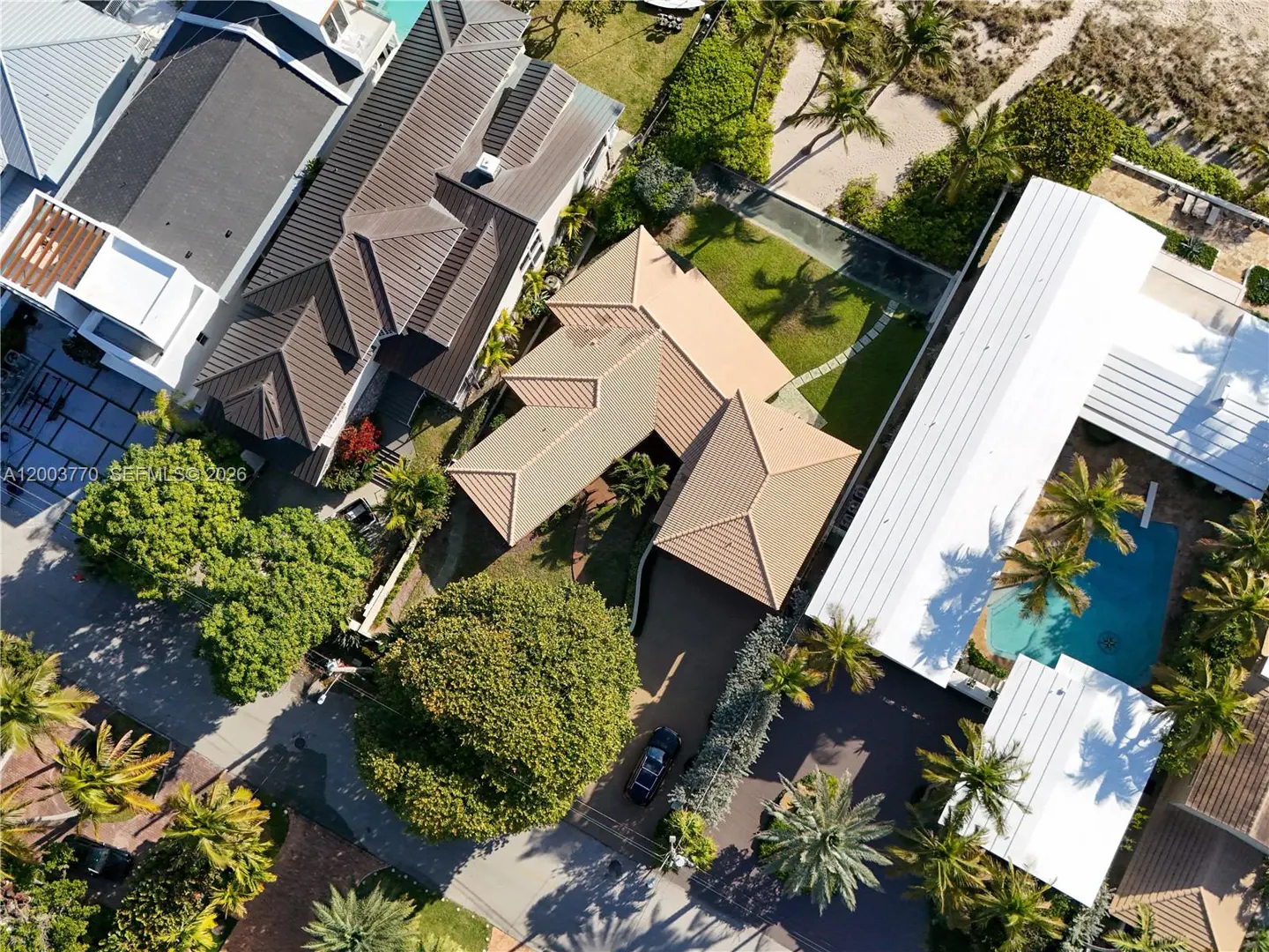 Aerial view of a tan-roofed house with a pool, palm trees, and a car in the driveway.