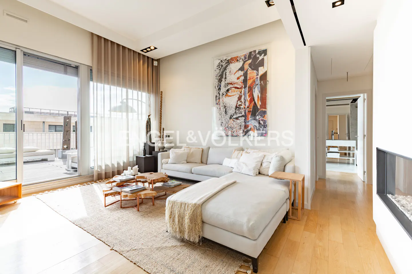 Bright living room with a white sectional sofa, wooden coffee tables, and a large abstract painting. Sliding glass doors lead to a balcony.
