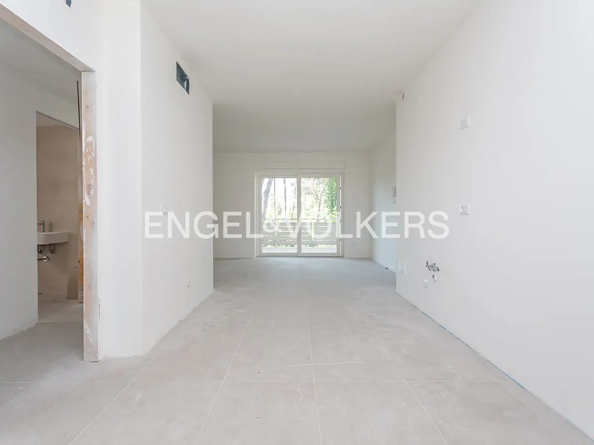 An empty, unfinished room with white walls, light tile floors, and a sliding glass door leading to a balcony.