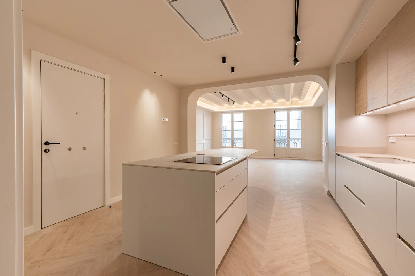 Bright, modern kitchen with white cabinets, island with cooktop, and herringbone wood floors. Large windows lead to a balcony.