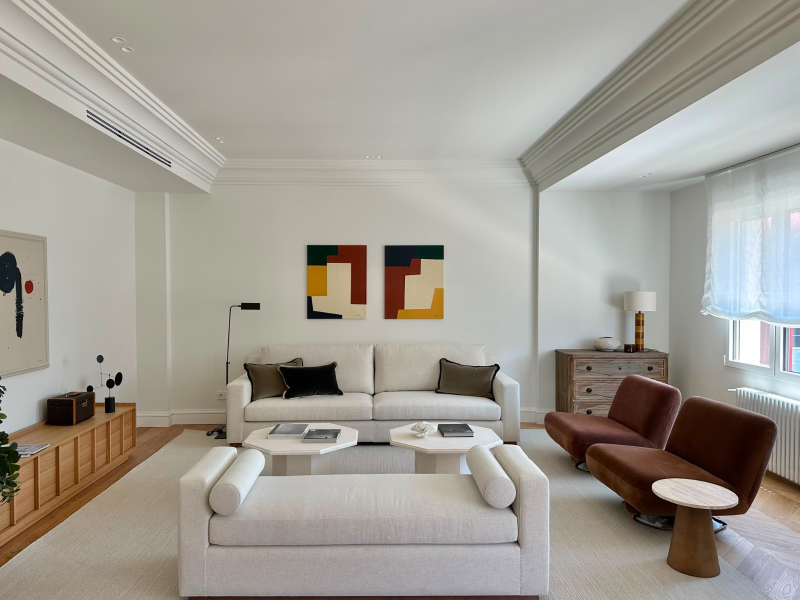 Modern living room with white sofa, two brown armchairs, white daybed, and abstract art on a white wall.