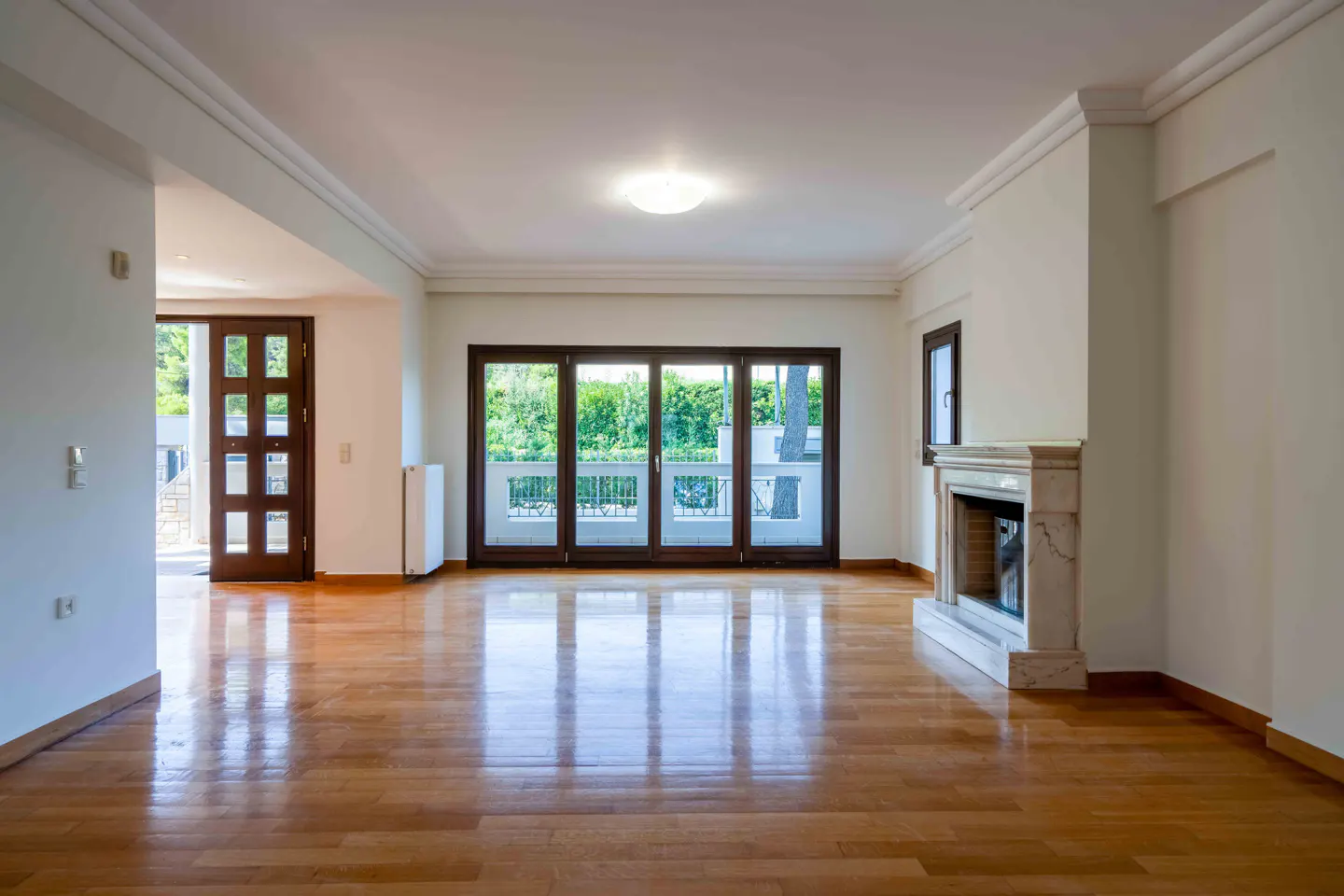 Bright, empty living room with hardwood floors, white walls, fireplace, and glass doors to a balcony.