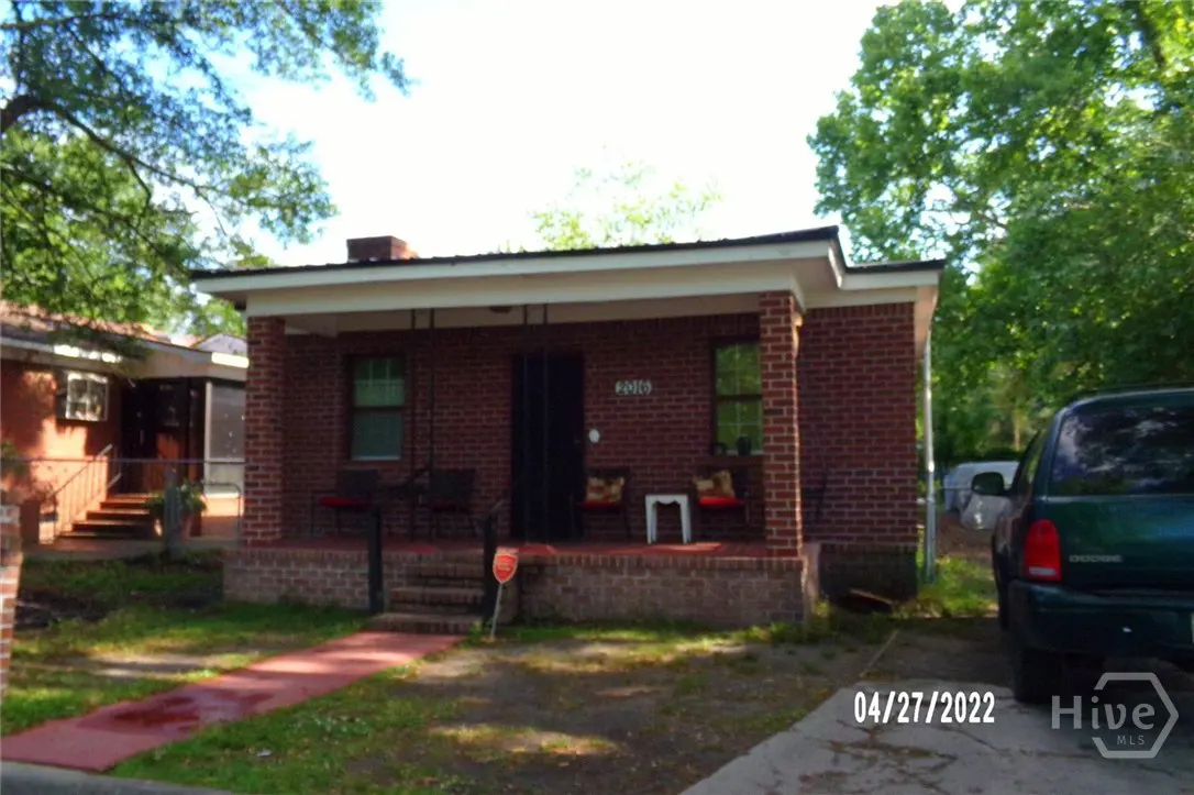 A red brick house with a porch and a green car parked in the driveway.