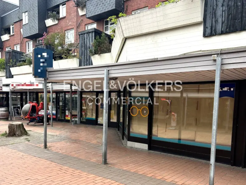 Exterior view of Engel & Völkers Commercial storefront with glass windows and a covered walkway. A red helicopter ride is visible nearby.