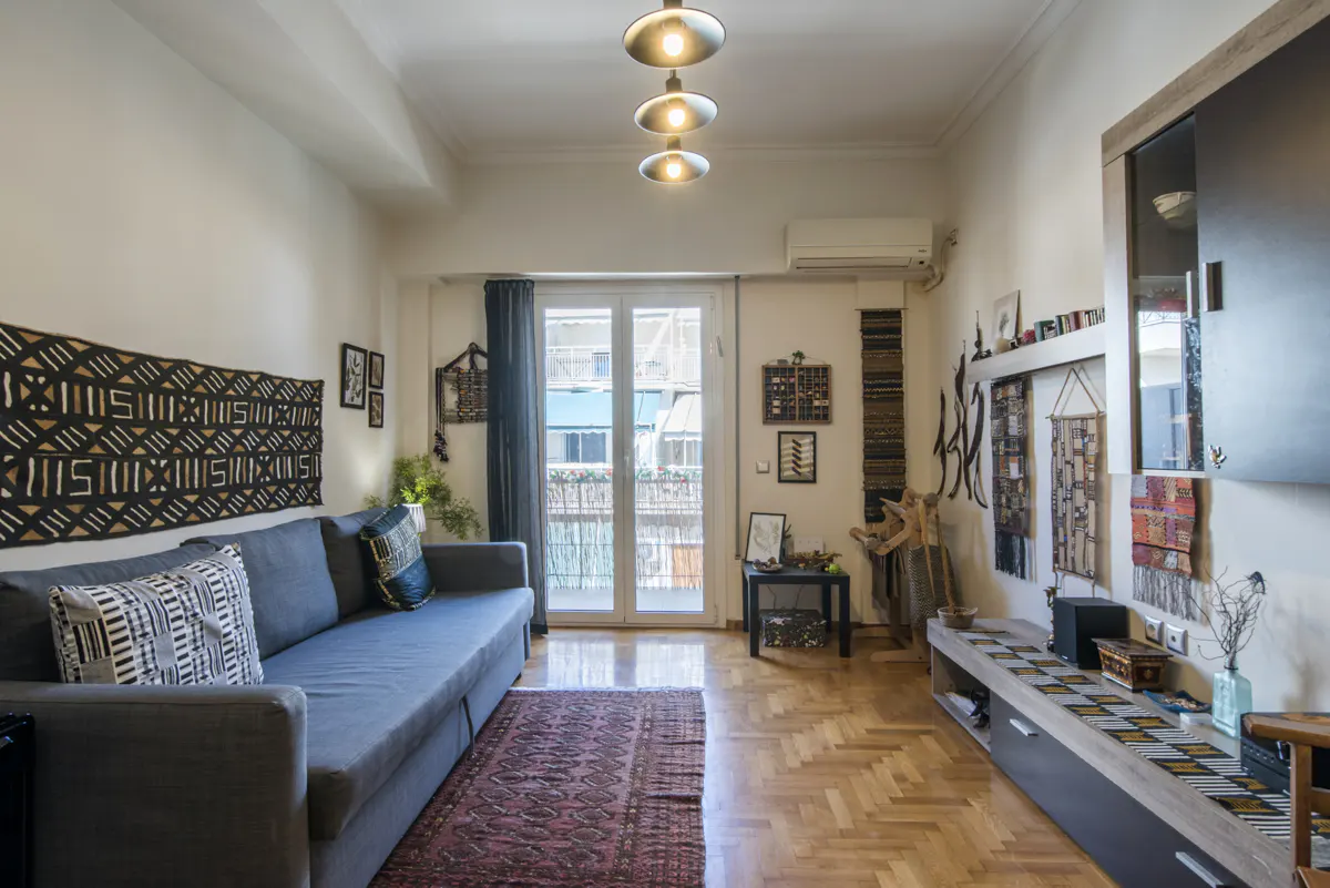 A living room with a gray sofa, patterned pillows, and a black and white tapestry on the wall. A red rug covers the wood floor.