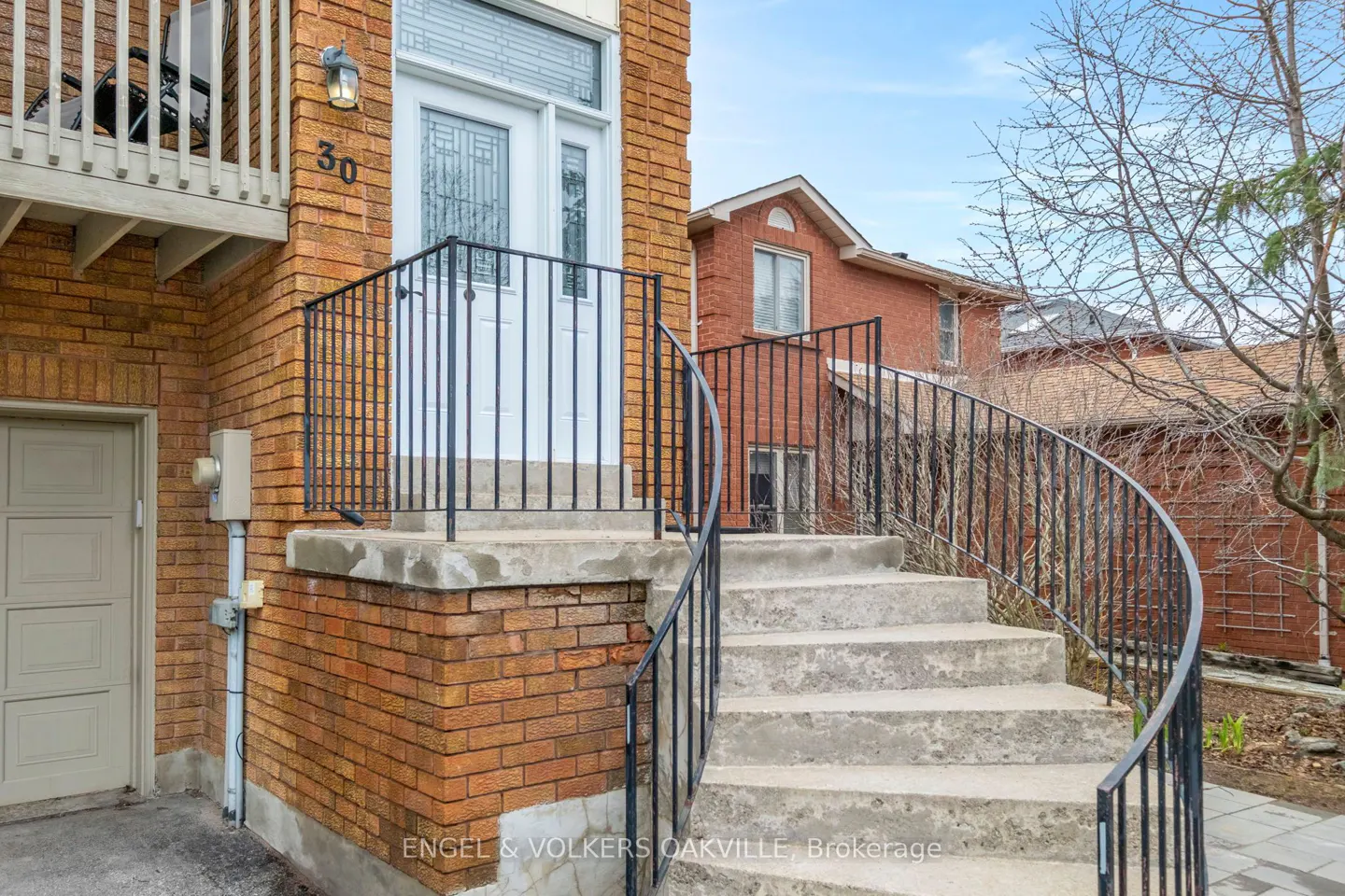 Brick house with concrete steps and black railing leading to a white front door. Number 30 is visible on the brick wall.