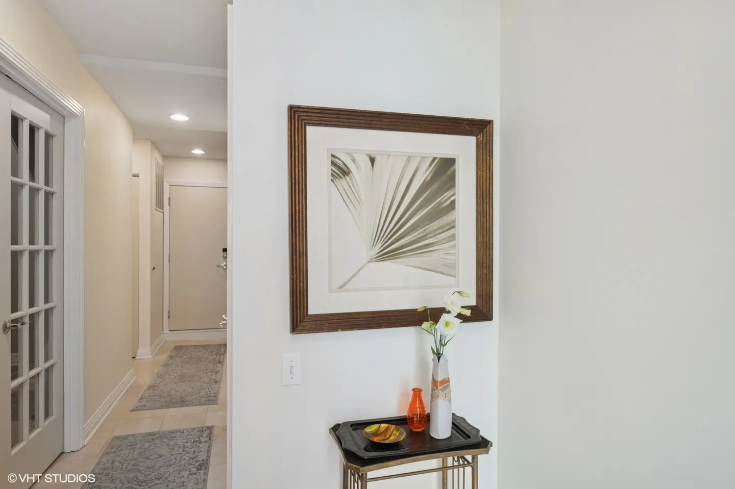 Hallway with a framed palm print above a small table with a vase of white flowers.
