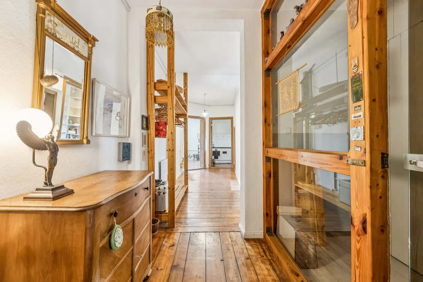 Hallway with wooden floors, white walls, and wooden shelving. A dresser with a lamp and mirror is on the left.