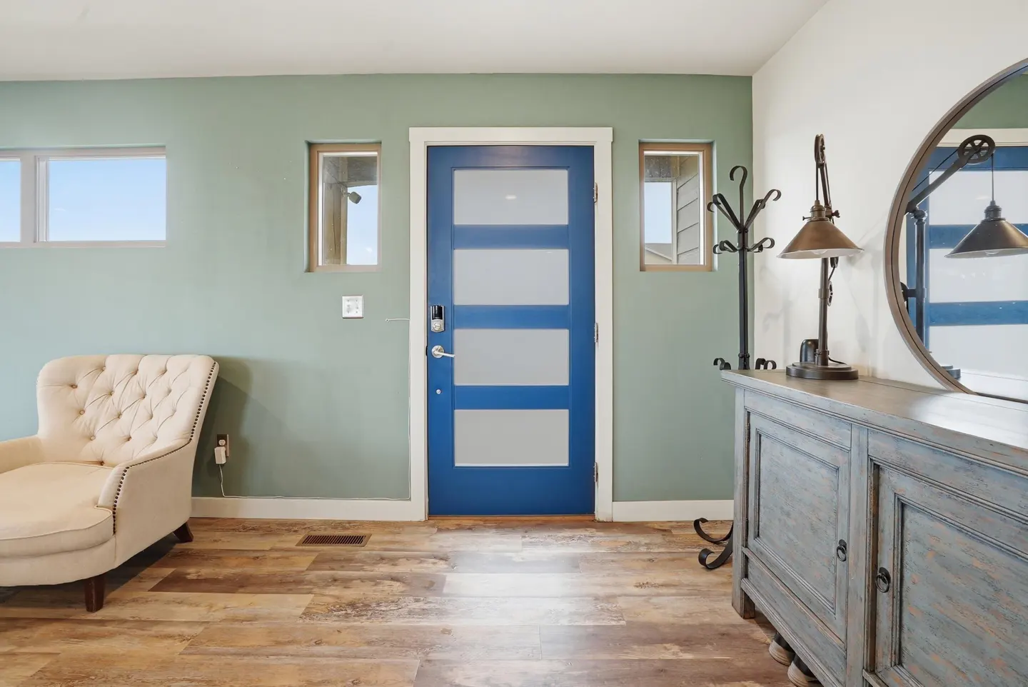 Entryway with sage green walls, a bright blue front door, a cream tufted chair, and a rustic blue wooden console table.