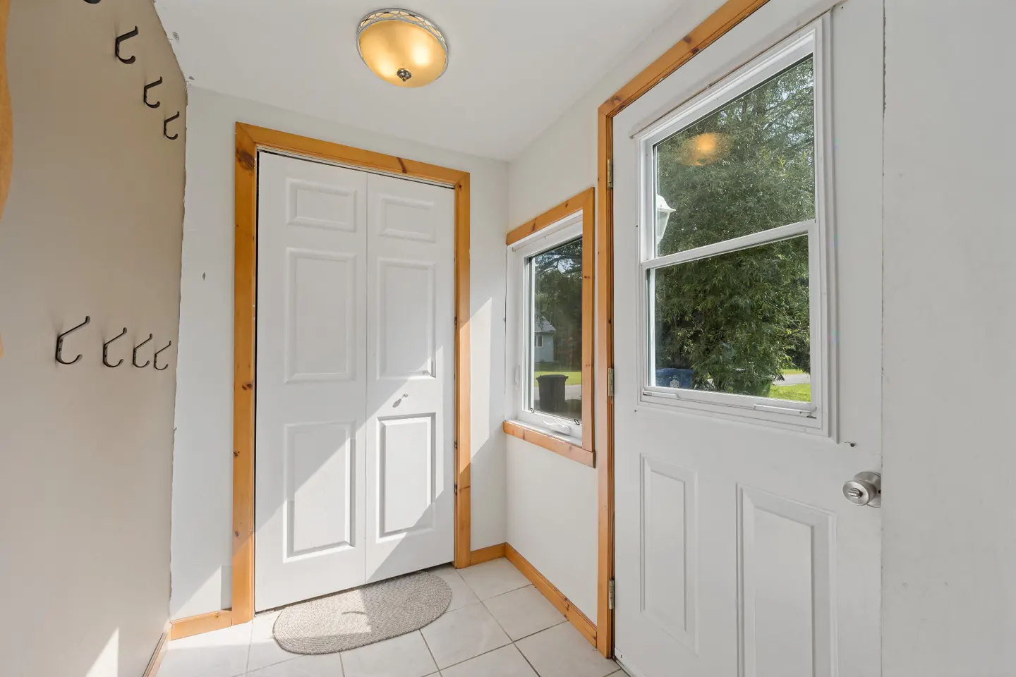 Entryway with white tiled floor, white double closet doors, a glass-paneled door, and wall hooks under a dome light.